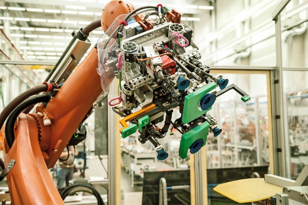 Nahaufnahme eines orangen Industrieroboters mit Sensoren, Kabeln und mehrteiliger Greifermechanik in moderner Fertigungsanlage